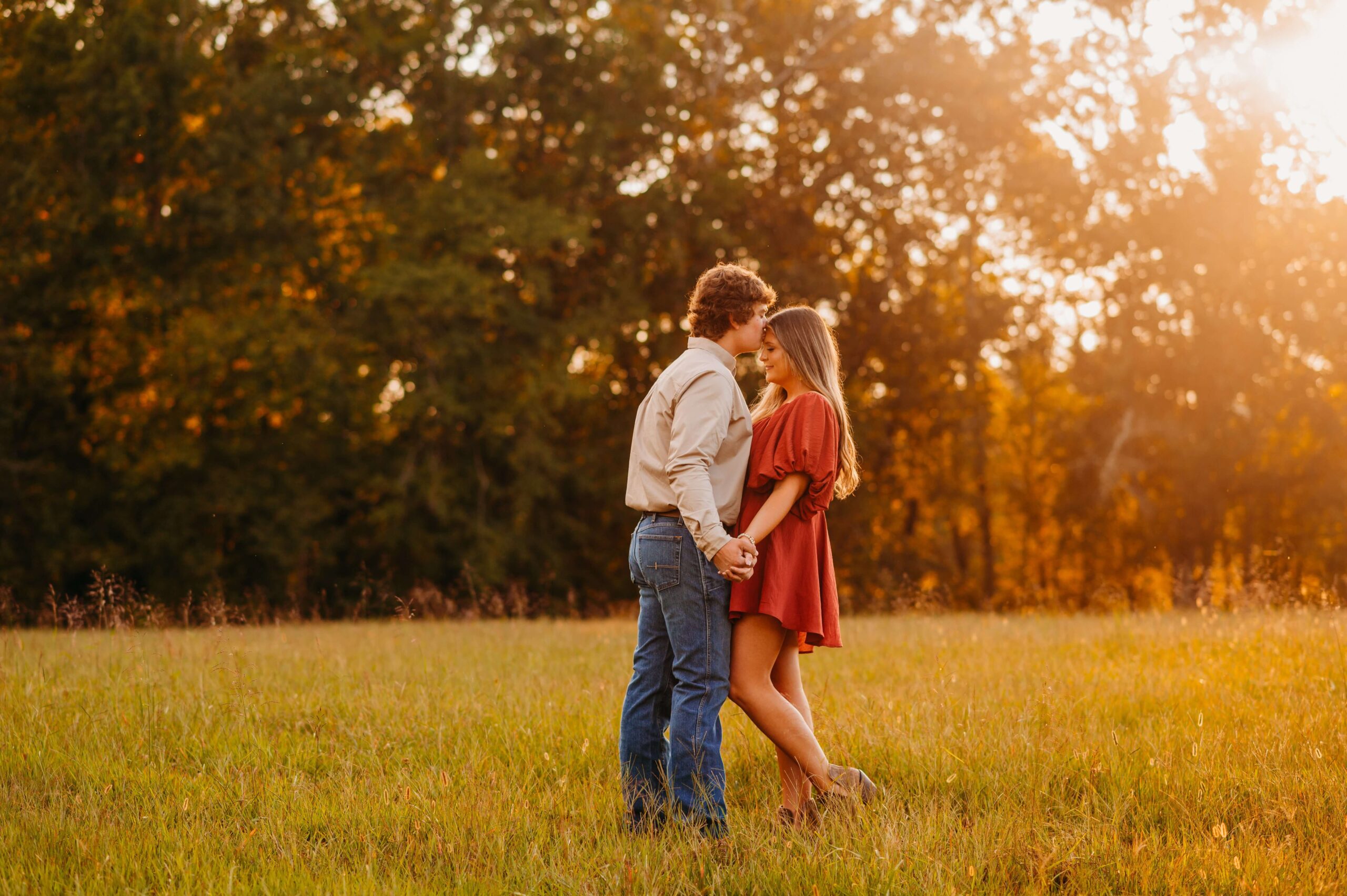 man kissing his fiancee's head and they stand in a field
