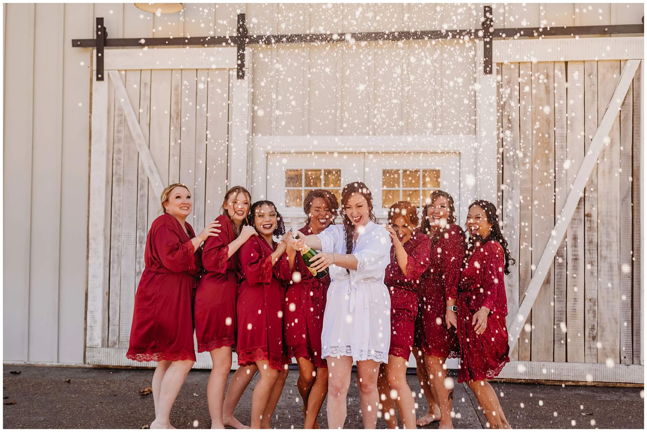 bride in white robe spraying champagne and bridesmaids in red robes