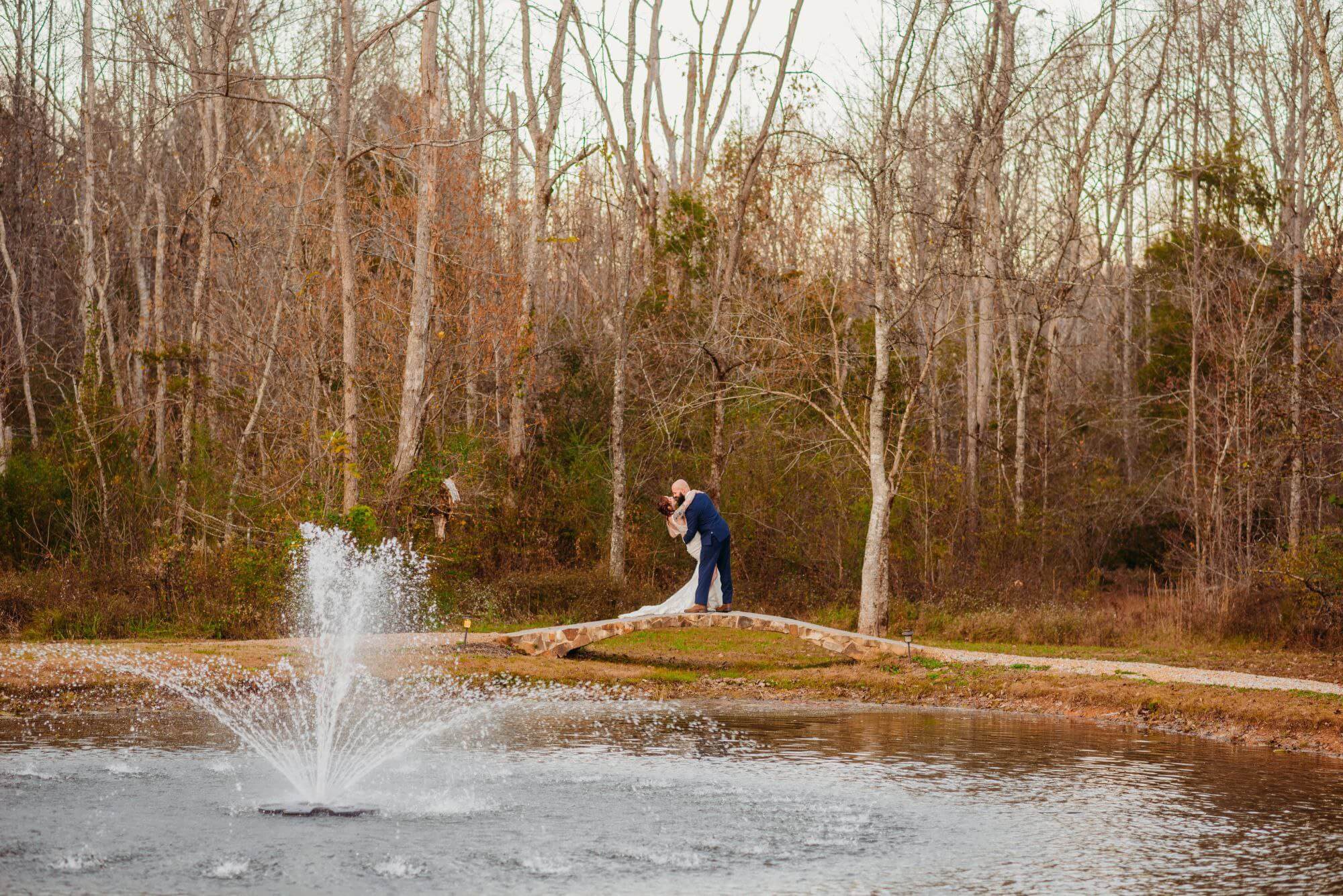 bride and groom dancing on the other side of Ramble Creek's pond with a fountain spraying in the foreground