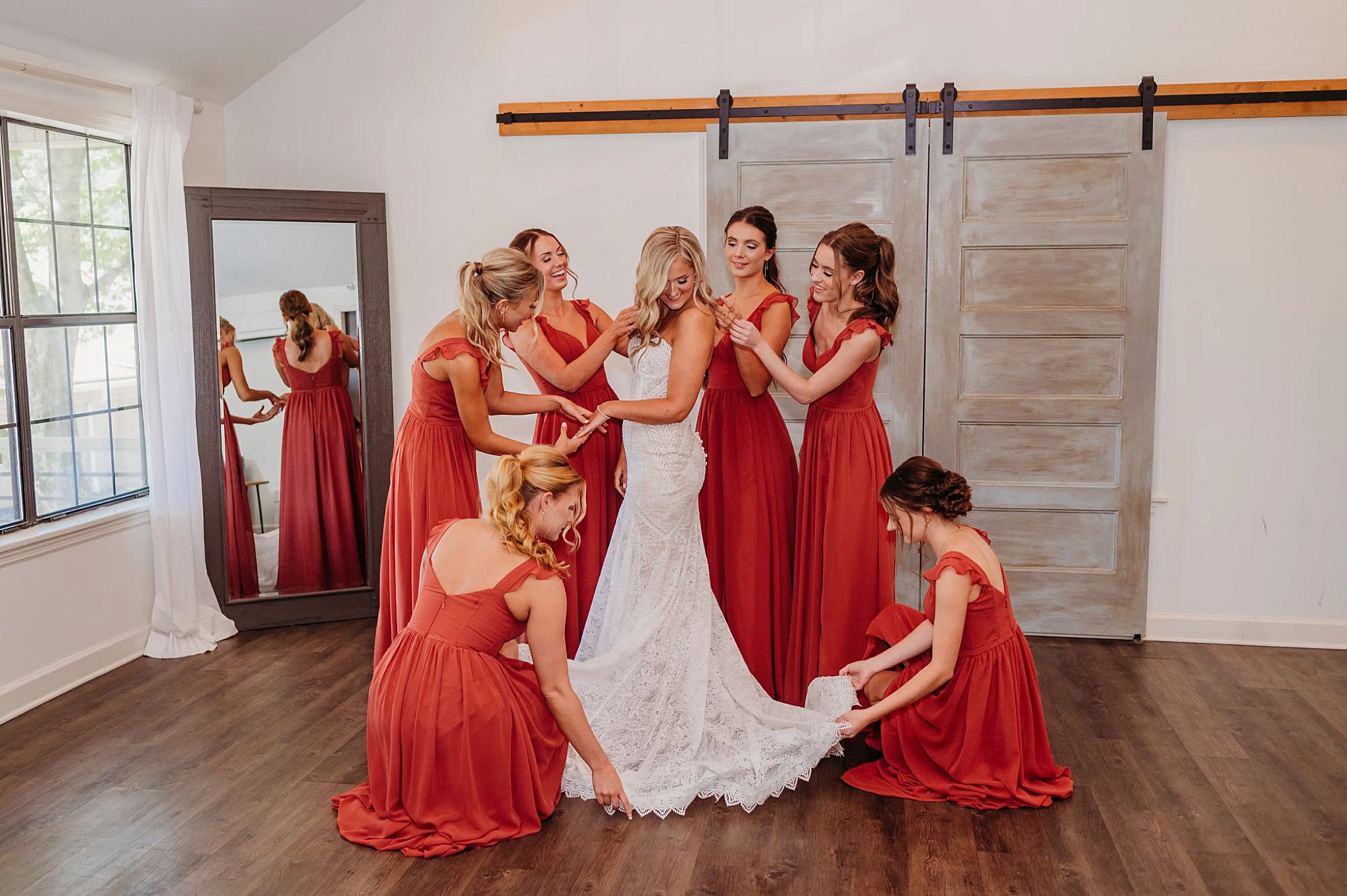 bridesmaids in maroon dressed surrounding bride and helping adjust her looks