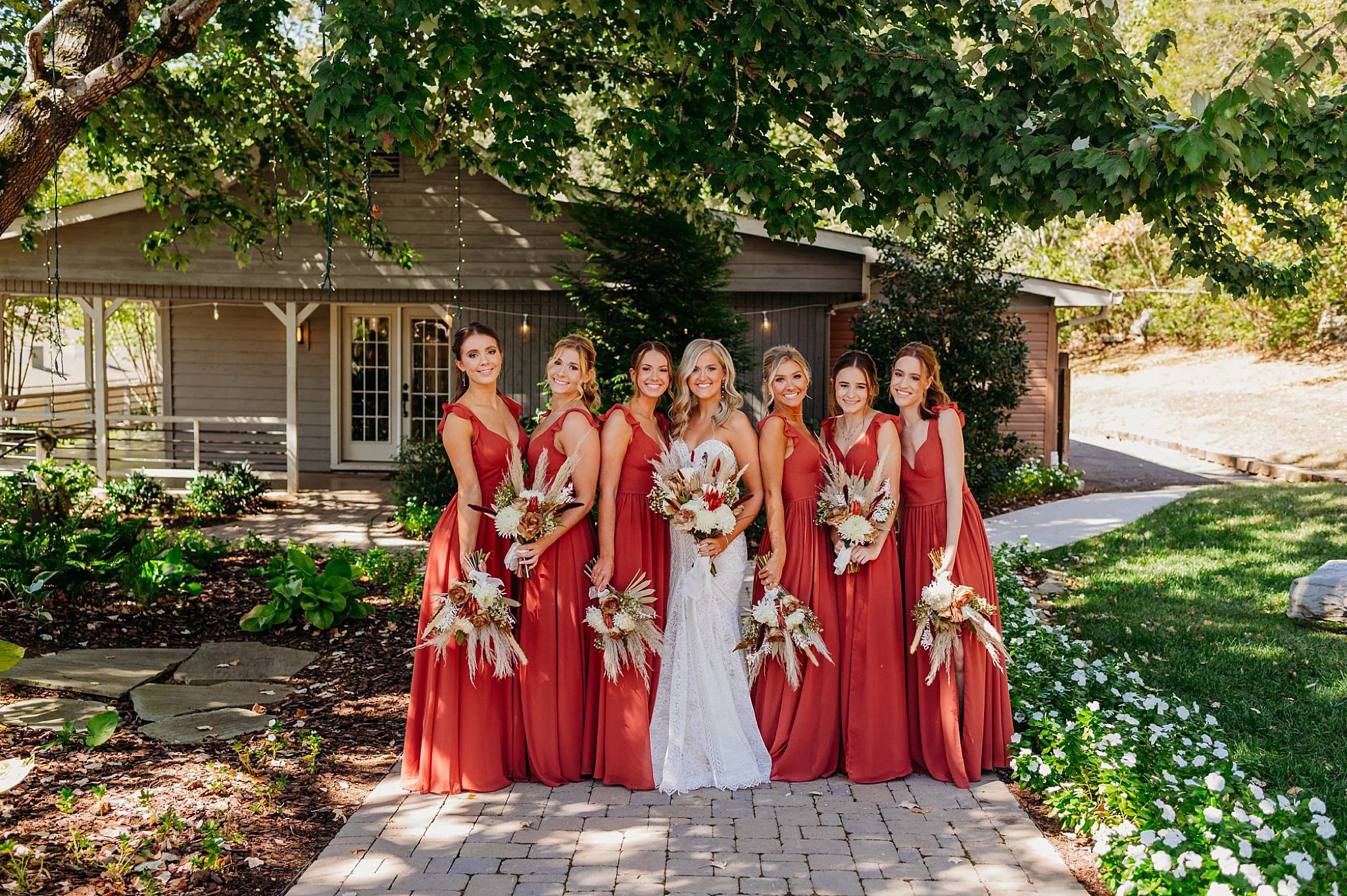 six maroon bridesmaids and a bride holding boho bouquets outside
