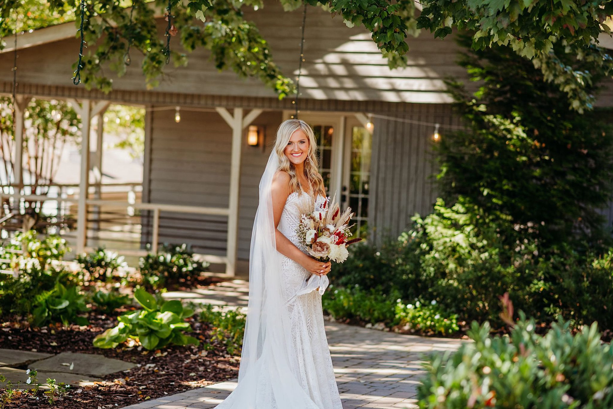 bride smiling with a boho wedding dress and bouquet in front of a cottage