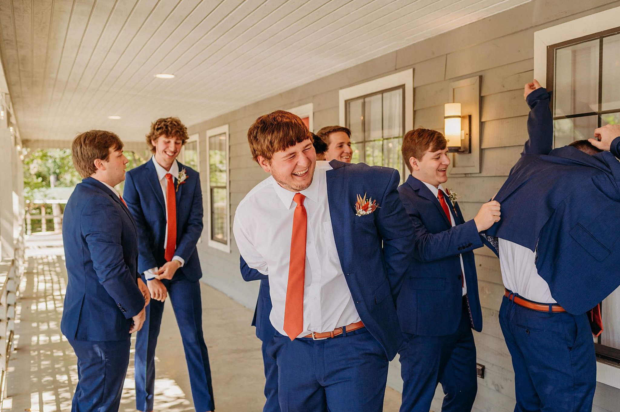 groomsmen putting on navy suits and laughing on a porch