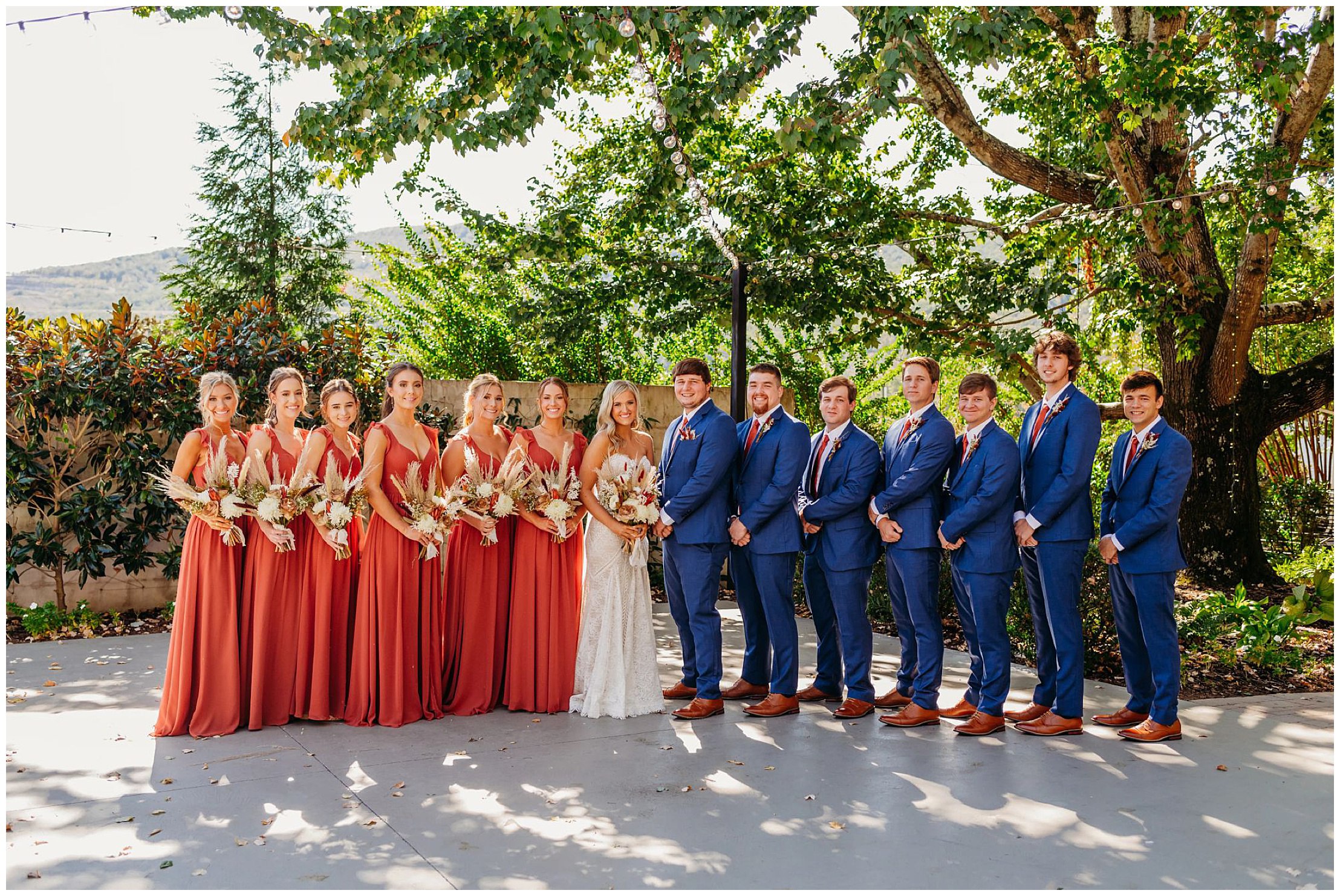 photo of bride and groom with maroon bridesmaids and navy groomsmen standing in a line on a patio