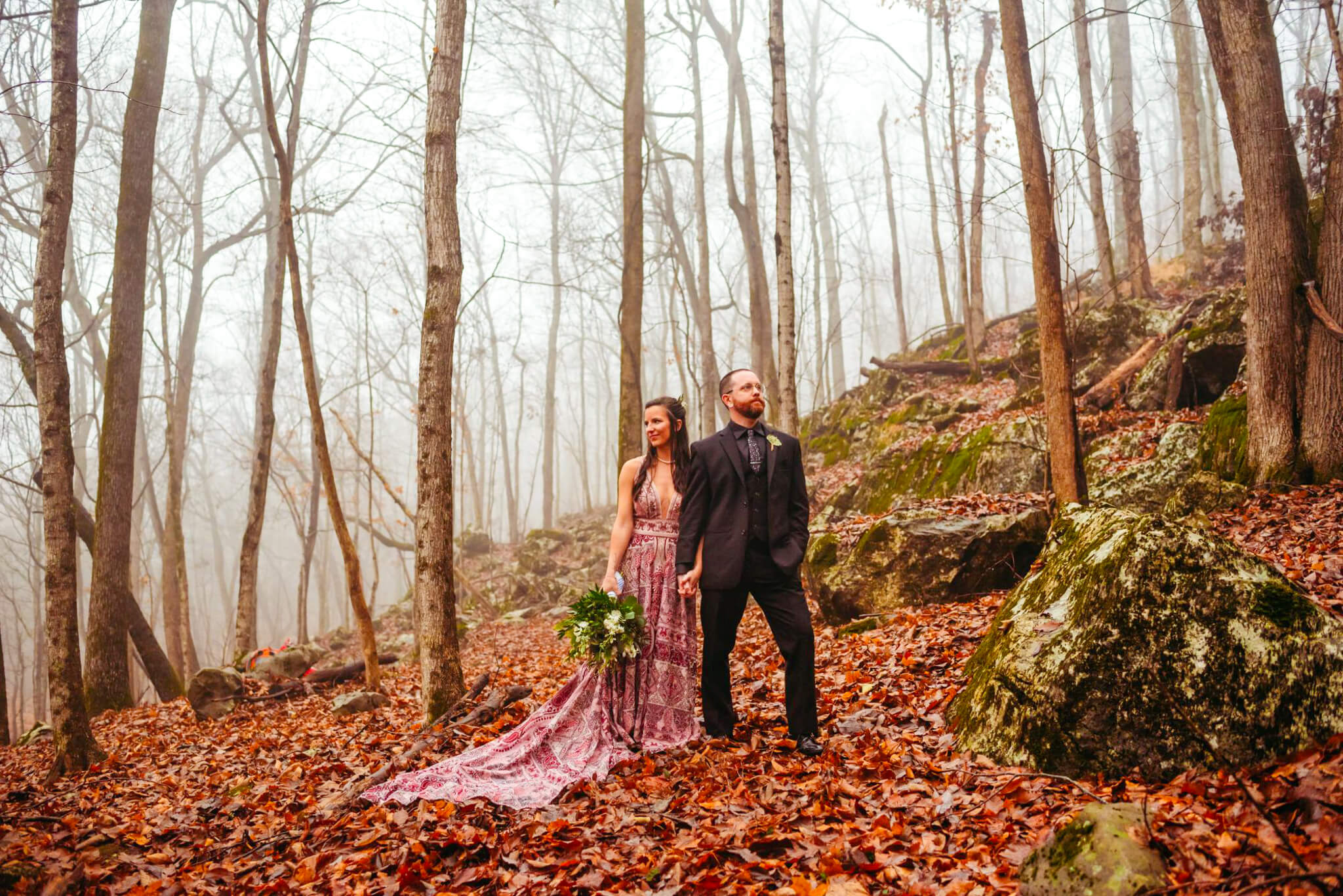 photo of a bride in a purple dress holding her groom's hand and looking into the forest on a foggy day